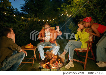 Teenager having fun at bonfire telling horror stories spending time at campsite 108472436