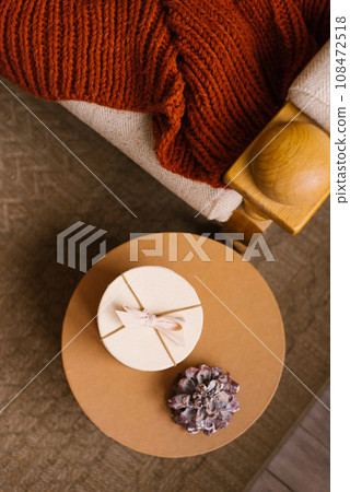 Christmas decor of a cozy home. A round box with a bow and a bump on the table near the sofa. Top view 108472518