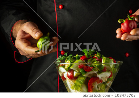 The cook prepares a salad with fresh vegetables in the restaurant kitchen. Vegetable dish in a breakfast bowl. Vegetarian healthy food concept 108473702