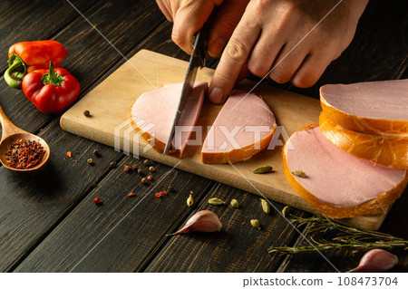 The cook cuts scalded sausage into small pieces for making sandwiches. Street food or fast food idea. Copy space The cook cuts scalded sausage into small pieces for making sandwiches. Street food or fast food idea. Copy space 108473704