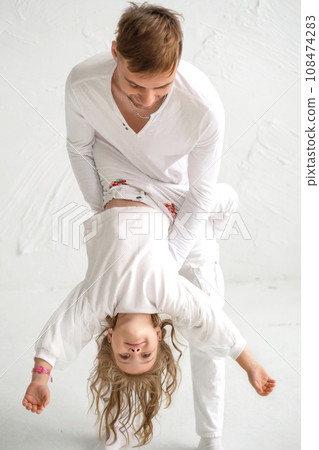 Dad is having fun playing with the child, lifting her in his arms and circling. The girl is hanging upside down Dad is having fun playing with the child, lifting her in his arms and circling. The girl is hanging upside down 108474283