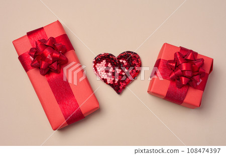 Red heart and boxes packed in red paper and tied with ribbon on a beige background Red heart and boxes packed in red paper and tied with ribbon on a beige background 108474397
