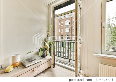 a living room with wood flooring and white walls, there is an open door that leads to the balcony 108475881