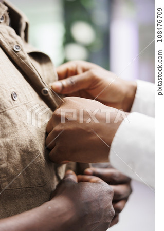 Shopping mall african american salesperson hands fastening shirt on buyer. Clothing store seller helping customer to wear trendy apparel to check size before making purchase close up 108476709