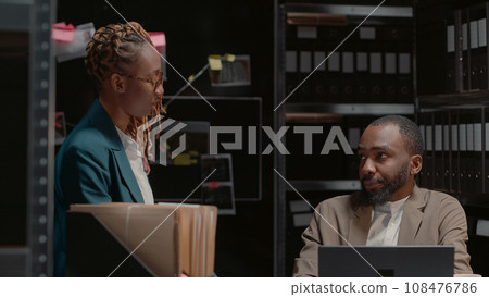 Two investigators studying forensic evidence on wall map, discussing criminal information in archive office. Team of detectives reading records in folders, doing background checks. Two investigators studying forensic evidence on wall map, discussing criminal information in archive office. Team of detectives reading records in folders, doing background checks. 108476786