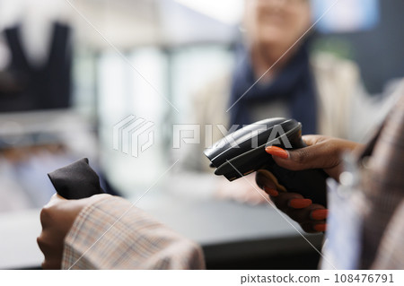African american worker scanning fashionable shirt using store scanner, preparing purchase for elderly shopaholic woman. Client buying casual wear in clothing store, commercial activity. Close up 108476791