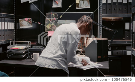 Law officer examining archived criminal records at police station, reviewing surveillance footage to uncover details. Private agent reading important case information on detective map. Law officer examining archived criminal records at police station, reviewing surveillance footage to uncover details. Private agent reading important case information on detective map. 108476846