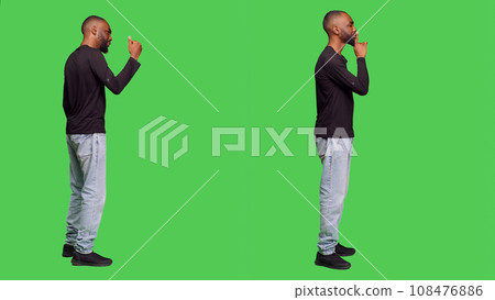 Confident man doing silence mute sign and calling over someone to join, showing privacy in studio. Young person showing hush gesture to keepy secret, raising hand and saying come over. Confident man doing silence mute sign and calling over someone to join, showing privacy in studio. Young person showing hush gesture to keepy secret, raising hand and saying come over. 108476886