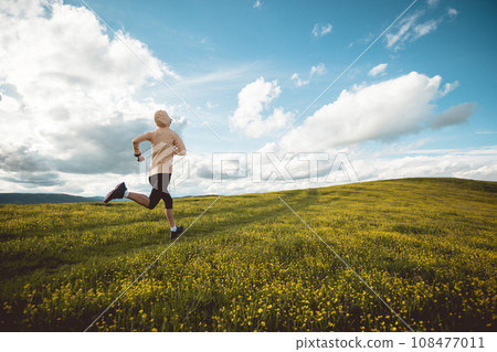 Woman trail runner cross country running at high altitude flowering mountain Woman trail runner cross country running at high altitude flowering mountain 108477011