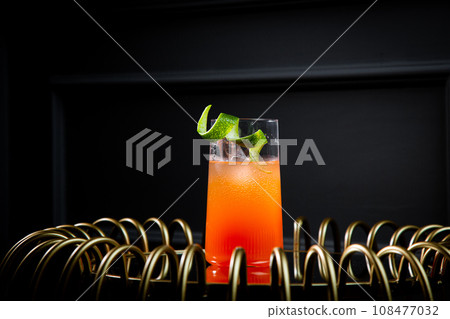 bright tropical cocktail with lime peel and gradient color in a transparent glass, side view bright tropical cocktail with lime peel and gradient color in a transparent glass, side view 108477032