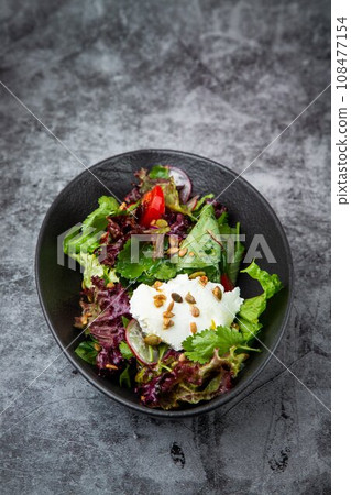 Green salad with radishes, tomatoes, herbs, cheese and nuts on a dark plate, top view Green salad with radishes, tomatoes, herbs, cheese and nuts on a dark plate, top view 108477154