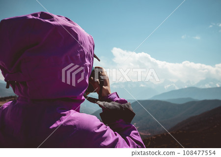 Woman hiker taking photo with camera in winter mountains Woman hiker taking photo with camera in winter mountains 108477554