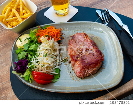 Piece of fried pork in sauce. Served with finely chopped carrots, lettuce, tomatoes and other vegetables. Belgian cuisine 108478891