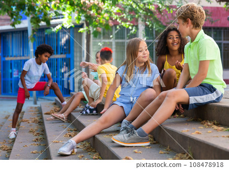 Happy tweenagers friends sitting on steps outdoors and chatting 108478918