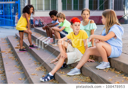 Positive tweenagers friendly blabbing while sitting on steps outdoors 108478953