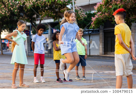 Cheerful preteen children playing chinese jump rope on city street 108479015