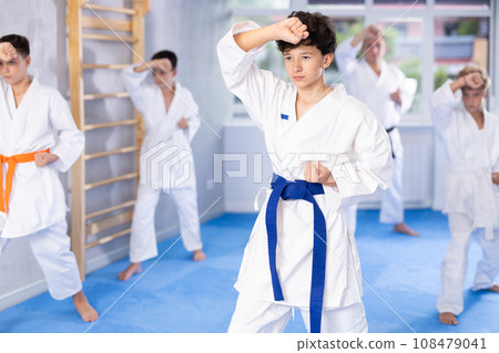 Teenager in kimono practicing punches during group martial arts workout 108479041