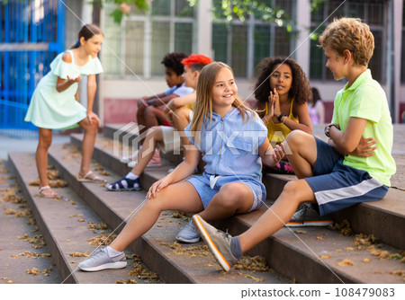 Cheerful preteen girls and boys sitting on steps outdoors and chatting 108479083