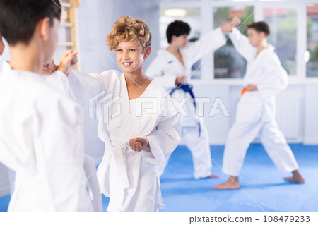 Diligent preteen attendee of karate classes fighting with his opponent in sports hall Diligent preteen attendee of karate classes fighting with his opponent in sports hall 108479233