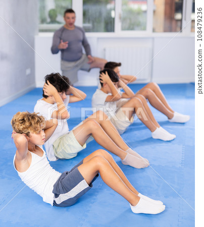 Underage boy practicing press in lying position with other attendees and trainer Underage boy practicing press in lying position with other attendees and trainer 108479236