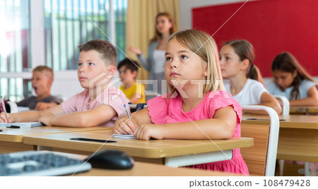 Focused small schoolgirl writing in workbook during lesson in class Focused small schoolgirl writing in workbook during lesson in class 108479428