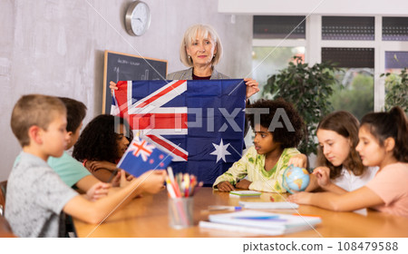 Elderly teacher holds the flag of Australia and tells the pupils the history of the country 108479588