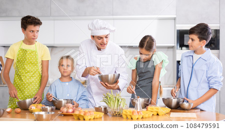 Sociable young chef leading culinary courses to group of tweens Sociable young chef leading culinary courses to group of tweens 108479591