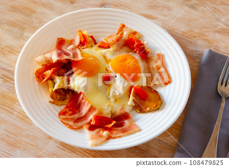 Delicious hearty dinner of sunny side eggs with baked potatoes and fried bacon pieces Delicious hearty dinner of sunny side eggs with baked potatoes and fried bacon pieces 108479825