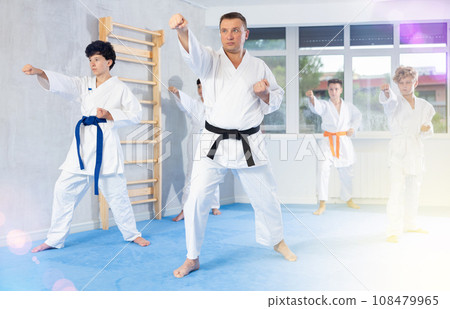 Karate master demonstrating hand strikes to teenagers during group kata Karate master demonstrating hand strikes to teenagers during group kata 108479965