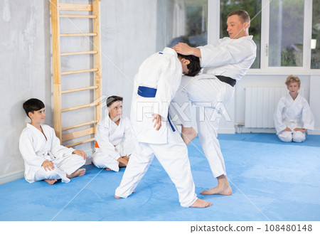 Instructor demonstrating karate techniques to group of teenagers in sparring with boy 108480148