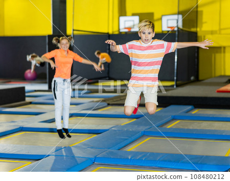 Joyful school-age boy in casual clothes bouncing on trampolines indoors in leisure sport center for kids 108480212