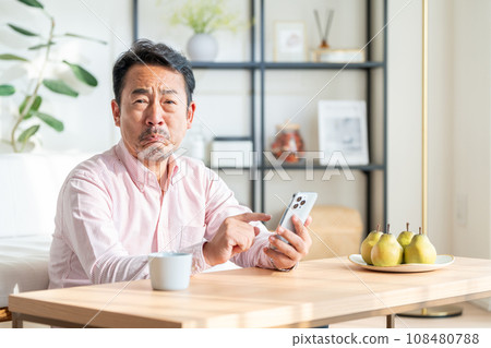 A senior man operates a smartphone in the living room. 108480788