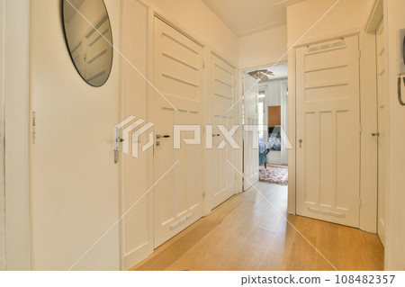 a long hallway with white doors and wood flooring on either side by side, looking into the living room 108482357
