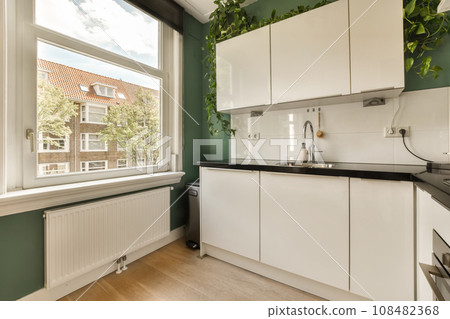 a kitchen area with green walls and white cupboards on either side of the window looking out onto the street 108482368