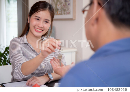 Young realtor woman real estate giving key house to hands customer while agreement. 108482936