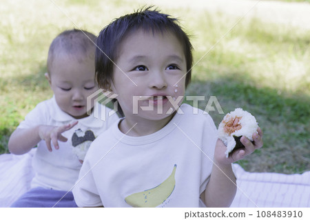 男孩兄弟在公園裡吃臉頰沾著米粒的飯糰 男孩兄弟在公園裡吃臉頰沾著米粒的飯糰 108483910