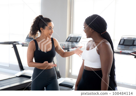 Two young woman talking in the gym, woman in sportswear and friend or coach relax. Two young woman talking in the gym, woman in sportswear and friend or coach relax. 108484114
