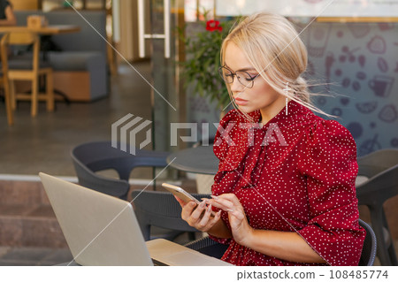 Beautiful woman works on laptop in coffee shop and using mobile phone in a red 108485774