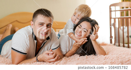 happy family lying on the bed and hugging, mom dad and little son happy family lying on the bed and hugging, mom dad and little son 108485782