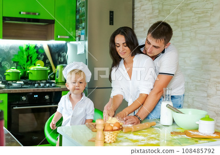 happy family mom and little son and dad are preparing dough in kitchen at table. products for dough are on table 108485792