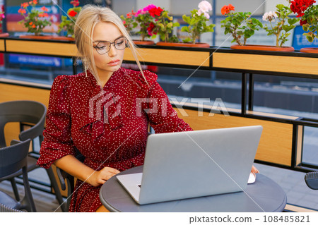 Beautiful woman works on laptop in coffee shop and using mobile phone in a red 108485821
