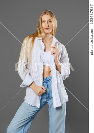Young woman posing with unbuttoned shirt on grey background Young woman posing with unbuttoned shirt on grey background 108487987