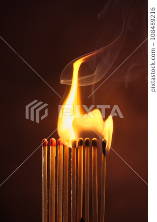 a row of matches are lit on a dark background a row of matches are lit on a dark background 108489216