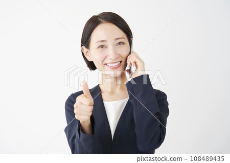 Middle-aged business woman giving a good sign while calling on a smartphone, white background Middle-aged business woman giving a good sign while calling on a smartphone, white background 108489435