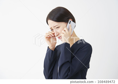 Middle-aged business woman crying while calling on a smartphone, white background 108489472