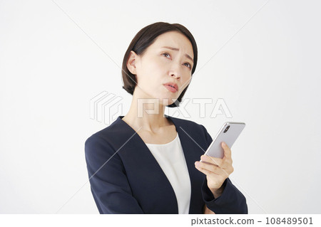 A worried middle-aged business woman holding a smartphone, white background 108489501