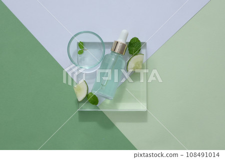 Mockup of dropper bottle on transparent podium with cucumber slices on pastel background. Templates for beauty product packaging based on cucumber, natural extract good for skin and hair 108491014