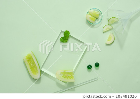 Some fresh cucumber slices decorated with transparent podium on green background. Blank space for display cosmetic product of cucumber extract, reducing sebum, helping to prevent acne from developing Some fresh cucumber slices decorated with transparent podium on green background. Blank space for display cosmetic product of cucumber extract, reducing sebum, helping to prevent acne from developing 108491020