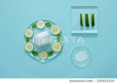 Mockup scene for advertising organic cosmetic with natural ingredient - cucumber. A cosmetic jar displayed on transparent podiums with cucumber slices and mint leaves on blue background Mockup scene for advertising organic cosmetic with natural ingredient - cucumber. A cosmetic jar displayed on transparent podiums with cucumber slices and mint leaves on blue background 108491030