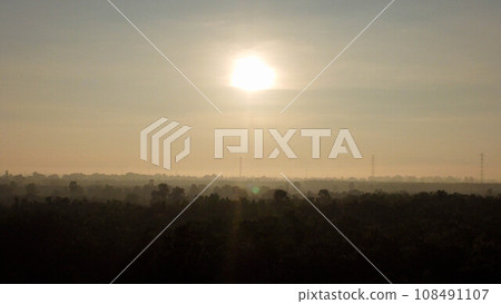 Aerial view of High voltage grid tower with wire cable at tree forest with fog in early morning. Colorful landscape with woods in fog, sunbeams, sky, forest in winter morning. Aerial view of High voltage grid tower with wire cable at tree forest with fog in early morning. Colorful landscape with woods in fog, sunbeams, sky, forest in winter morning. 108491107